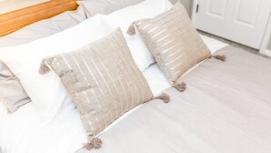 A bed with white bedding and two beige pillows with tassels.