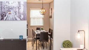 A modern dining area with a table set for four, a hanging light fixture, and a view of the street through a window.