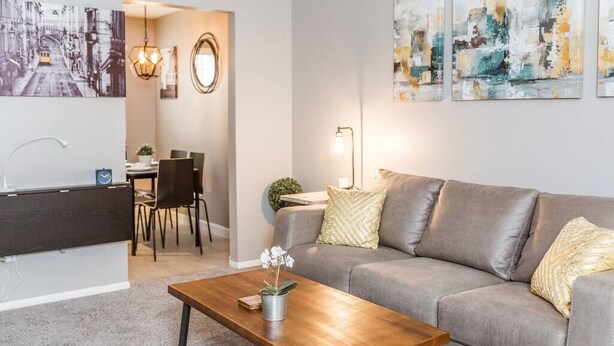 A modern living room with a grey sofa, a wooden coffee table, and a dining area with chairs and a table.