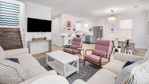 Een moderne woonkamer met een flatscreen televisie, twee roze fauteuils, een witte bank en een kleine salontafel.
