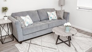 A modern living room with a grey sofa, patterned cushions, a round coffee table, a small side table, and a potted plant. - Newly Renovated (6A) OSU/Central ❤NearEVERYTHING (Columbus)