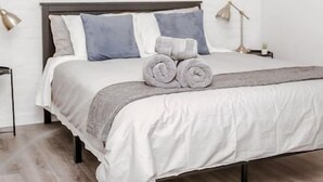 A neatly made bed with a gray blanket and rolled towels, a ceiling fan, and a wall-mounted abstract painting. - Newly Renovated (6A) OSU/Central ❤NearEVERYTHING (Columbus)