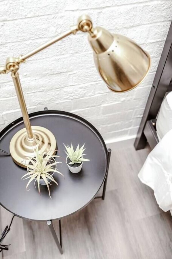A round table with a gold lamp, two potted plants, and a white brick wall in the background.