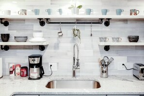 A kitchen with a stainless steel sink, a coffee maker, and various kitchen utensils on the countertop.