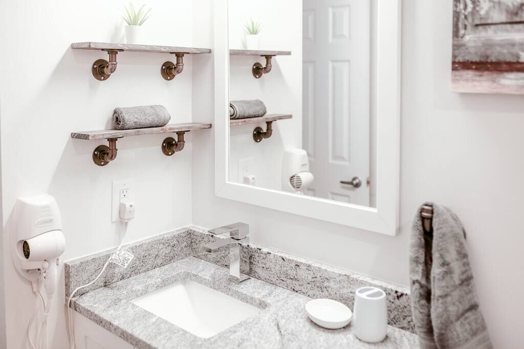 A bathroom with a granite countertop, a white sink, a mirror, and two wooden shelves with towels.