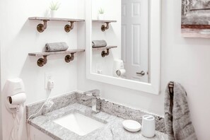 Ein Badezimmer mit Granitplatte, einem weißen Waschbecken, einem Spiegel und zwei Holzböden mit Handtüchern.