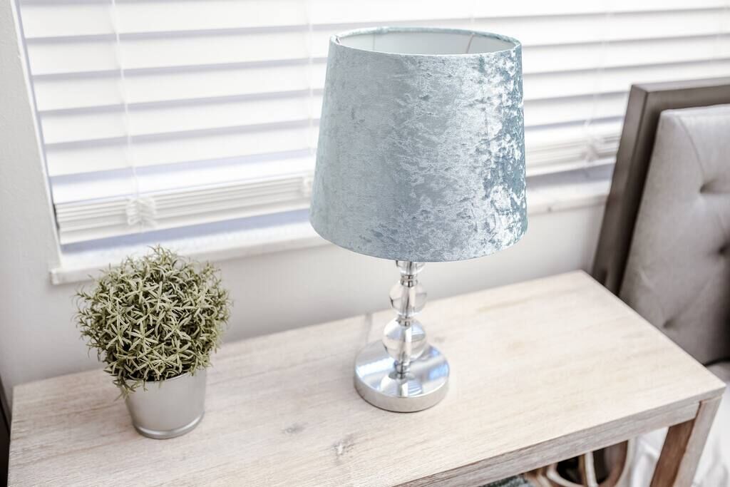 A lamp with a textured shade on a wooden table next to a potted plant.
