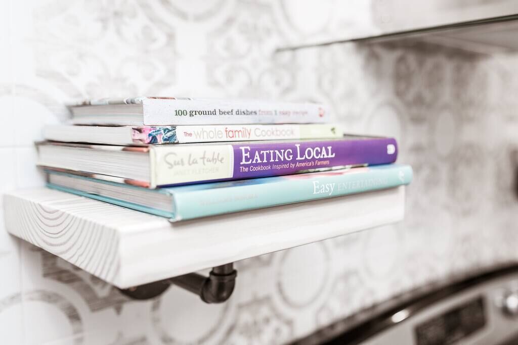 Una pila de libros de cocina sobre un estante blanco.