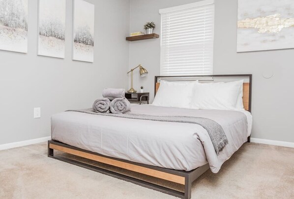 A bedroom with a bed, a nightstand, a lamp, and wall art.