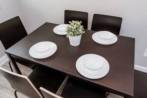 A rectangular dining table with four white plates and a small white vase with green foliage.