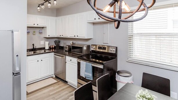 A modern kitchen with white cabinets, stainless steel appliances, and a unique circular chandelier.