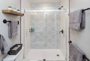 A modern bathroom with a shower, patterned tiles, a toilet, and towels on hooks.
