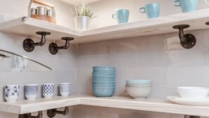 A kitchen with white tiled walls, two white shelves with blue and white dishes, and a hanging pot rack. - Newly Renovated (E) OSU/Central ❤Near EVERYTHING (Columbus)