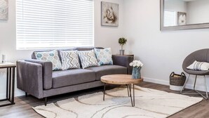 A modern living room with a grey sofa, a round wooden coffee table, and a large window with blinds. - Newly Renovated (E) OSU/Central ❤Near EVERYTHING (Columbus)