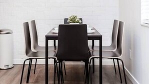 A dining area with a white brick wall, a geometric pendant light, and a framed picture above the table. - Newly Renovated (E) OSU/Central ❤Near EVERYTHING (Columbus)
