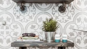 Una cocina con papel tapiz estampado, una estantería con una planta, saleros y pimenteros, y una pila de libros.