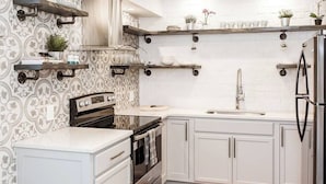 Una cocina moderna con gabinetes blancos, electrodomésticos de acero inoxidable y estantes decorativos.