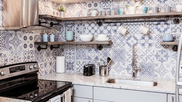 Une cuisine avec des carreaux décoratifs, un fourneau, un évier et des étagères remplies d’ustensiles de cuisine.