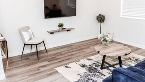 Un salon moderne avec un téléviseur à écran plat fixé au mur, une table basse ronde, un canapé bleu et un tapis à motifs.
