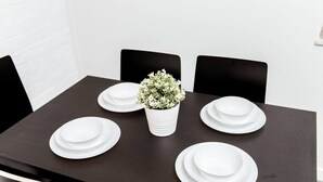 Une table à manger avec de l’assiette blanche et un vase blanc rempli de fleurs, le tout placé sur une table sombre et entouré de chaises noires.
