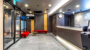 A modern hotel lobby with a reception desk, a red bench, and a glass wall. - HOTEL LiVEMAX OKAZAKI (Okazaki)