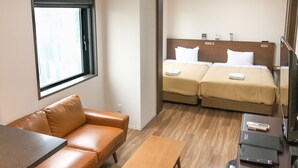 A hotel room with a brown leather sofa, a wooden table, two beds with beige bedding, a window, and a television on a wooden stand. - Hotel LiveMax Nagoya-Shinkansenguchi (Nagoya)