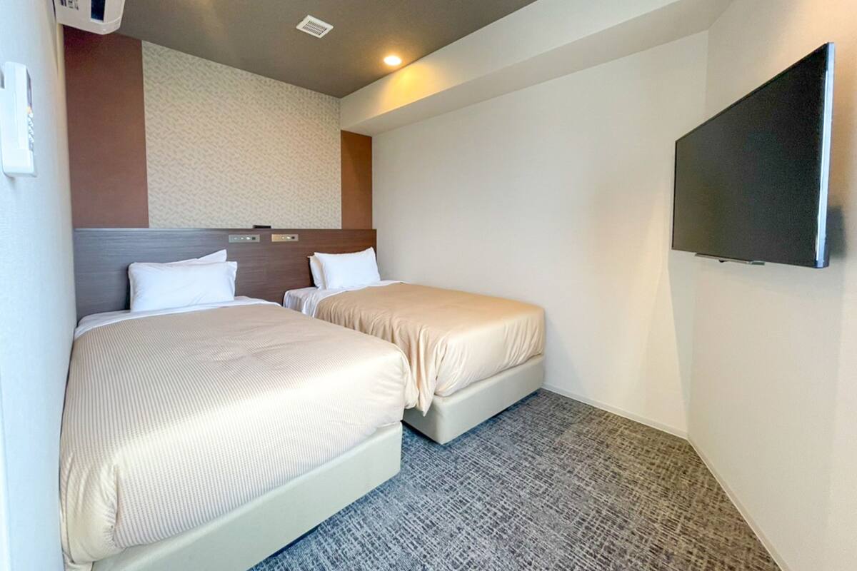Ein Hotelzimmer mit zwei Betten, einem an der Wand befestigten Flachbildfernseher und einem gemusterten Teppich.