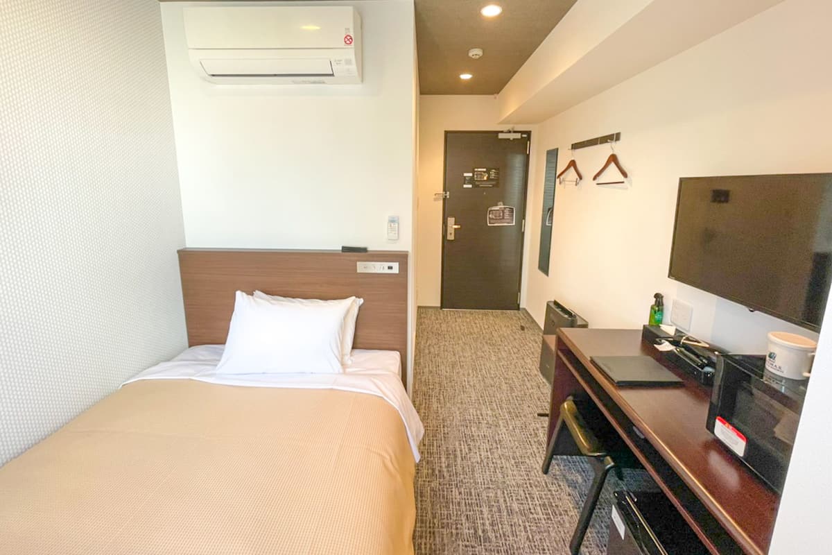 Ein Hotelzimmer mit Bett, Schreibtisch, Fernseher und Klimaanlage.