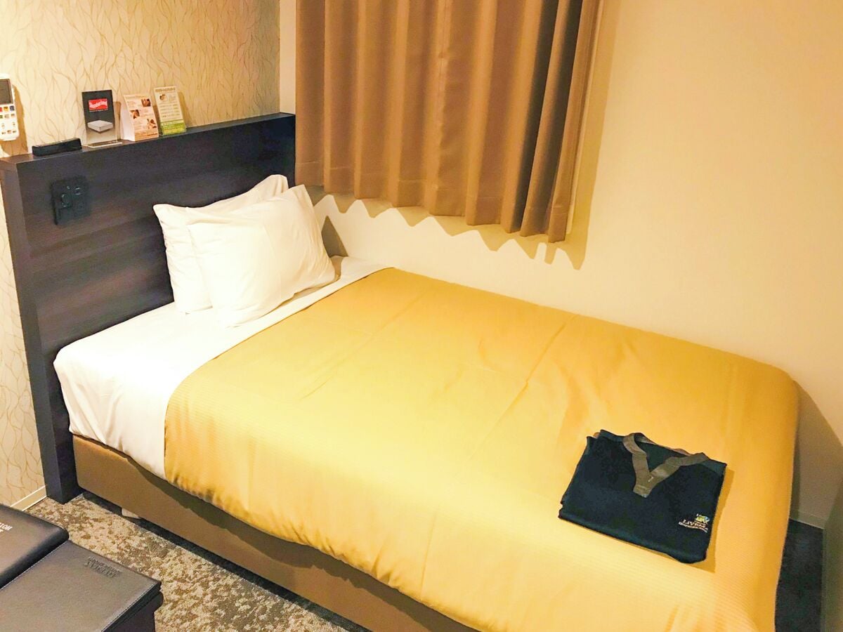 Ein Hotelzimmer mit Bett, Nachttisch, Telefon und einem Fenster mit Vorhängen.