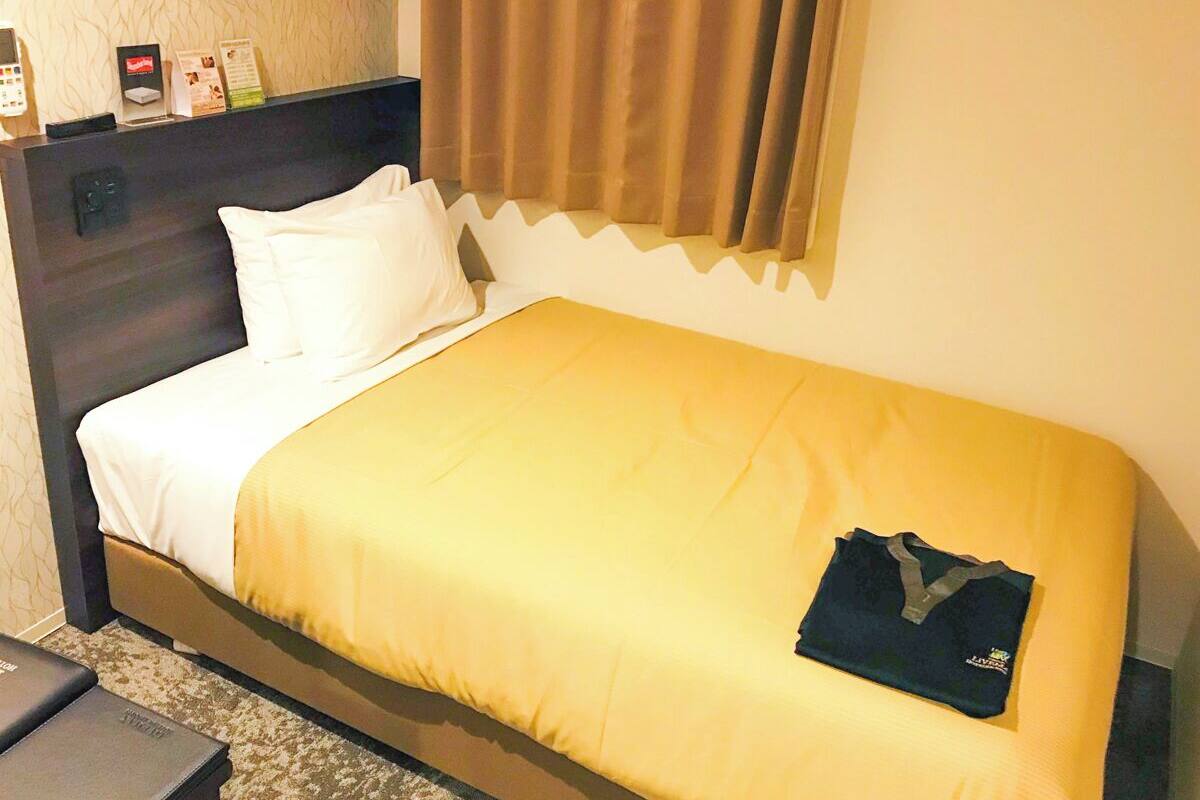 Ein Hotelzimmer mit Bett, Nachttisch, Telefon und einem Fenster mit Vorhängen.