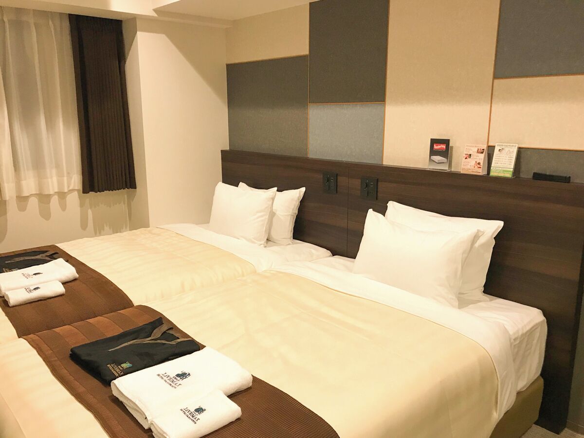 Ein Hotelzimmer mit einem großen Bett, zwei Kissen, einem Kopfteil und einem Nachttisch mit einem gefalteten Handtuch und einem schwarzen Gegenstand.