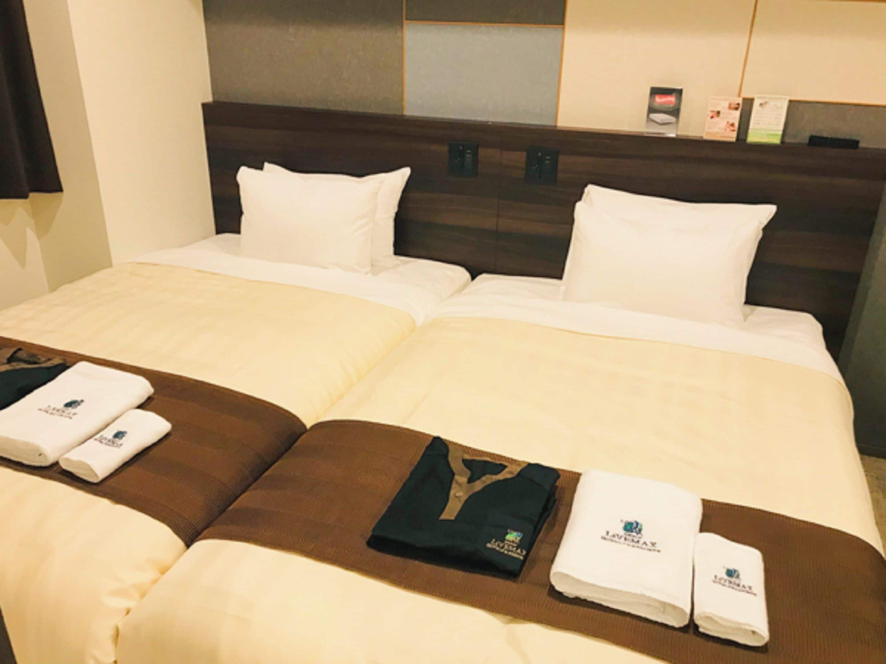 Ein Hotelzimmer mit einem Doppelbett, zwei Kissen, einem Kopfteil und einem Nachttisch mit Lampe und kleinem Tisch.