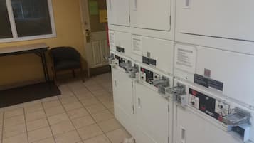 Een wasserette met gestapelde wasmachines, een bankje en een deur naar een andere ruimte.