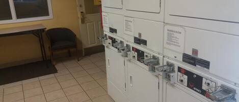 A laundry room with stacked washing machines, a bench, and a door leading to another room.
