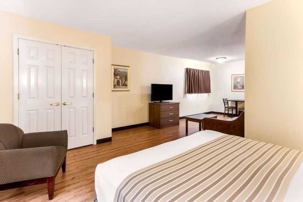 Una habitació d'hotel amb llit, escriptori, cadira, televisió i armari.