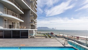 Blick auf einen Pool mit Holzterrasse, Meer und Bergen.