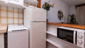 A compact kitchen with a white refrigerator, a microwave, and a built-in oven. There is a wooden countertop and a vase with flowers on the wall.
