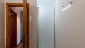 A hallway leading to a glass-enclosed shower area with a wooden door and tiled walls.
