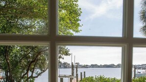 A view through a window of a grassy area with a body of water and a dock in the background. - Rare last-minute DISCOUNT in Indian Rocks Beach! Renovated 3BR WATERFRONT single family home with private dock sleeps 8, WALK to the sugar-white sand beach, Includes paddle board, beach chairs, wagon & umbrellas.  3bdrm, 2 bthrm, sleeps up to 8. (Indian Rocks Beach)