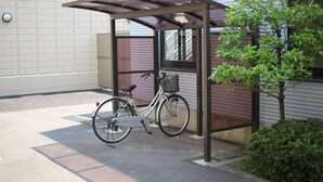 A covered bicycle parking area with a bike rack, a small tree, and a building with a brick facade. - Isesaki Station Hotel (Isesaki)