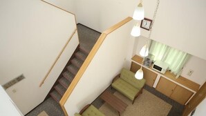 A staircase leading to a living area with a sofa, a small table, and a kitchen area with a sink and cabinets. - Isesaki Station Hotel (Isesaki)