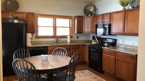 Una cocina con armarios de madera, encimera de granito, una mesa de comedor con sillas, refrigerador, estufa y microondas.