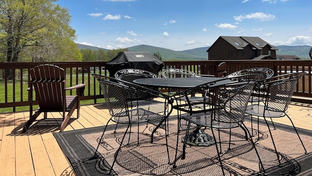 Una terraza con mobiliario exterior, incluyendo sillas y una mesa, con vistas a un paisaje pintoresco con montañas y una casa al fondo.