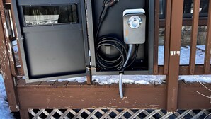 Un cuadro eléctrico exterior con un puerto de carga y un cable.