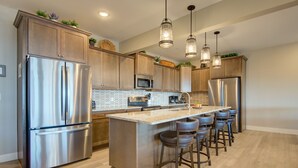 A modern kitchen with stainless steel appliances, wooden cabinets, and a central island with bar stools. - Stay awhile and prolong your smile (Branson)