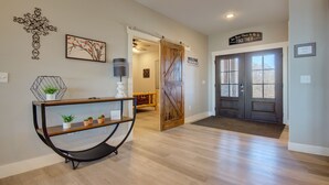 A hallway with a wooden floor, a black metal console table with plants, a wall-mounted tree decoration, and a door with a "WELCOME" sign. - Stay awhile and prolong your smile (Branson)