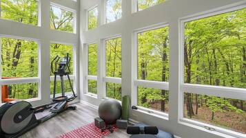 A gym with exercise equipment, a yoga mat, and large windows overlooking a forest.