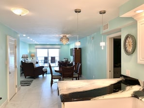 A spacious room with a dining area, a kitchen with a marble countertop, and a large window providing natural light.