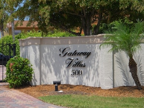 A sign for Gateway Villas, number 500, with a brick pathway and greenery in the foreground.