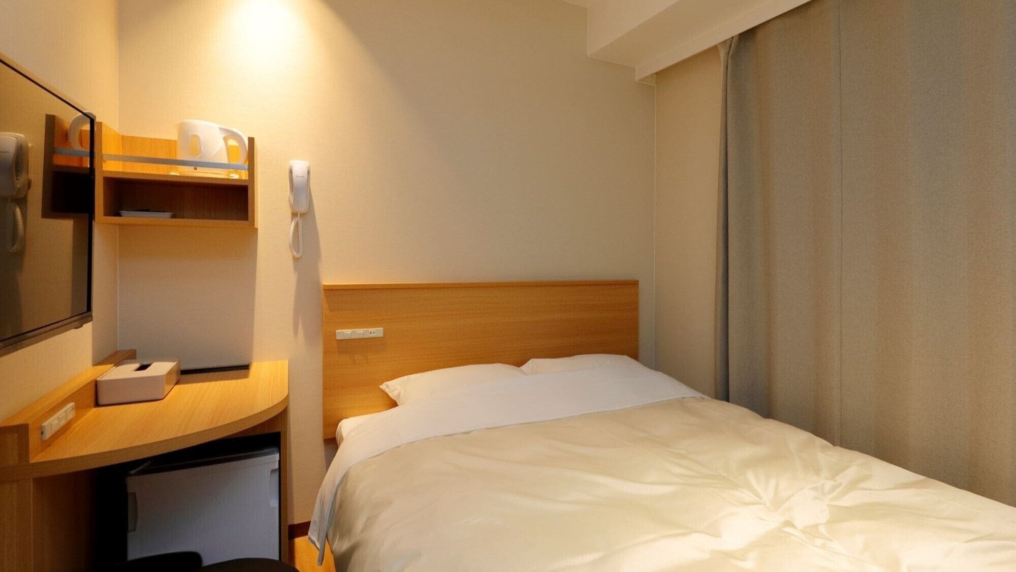 Een hotelkamer met een bed, een bureau met telefoon, een spiegel en een klein plankje met toiletartikelen.